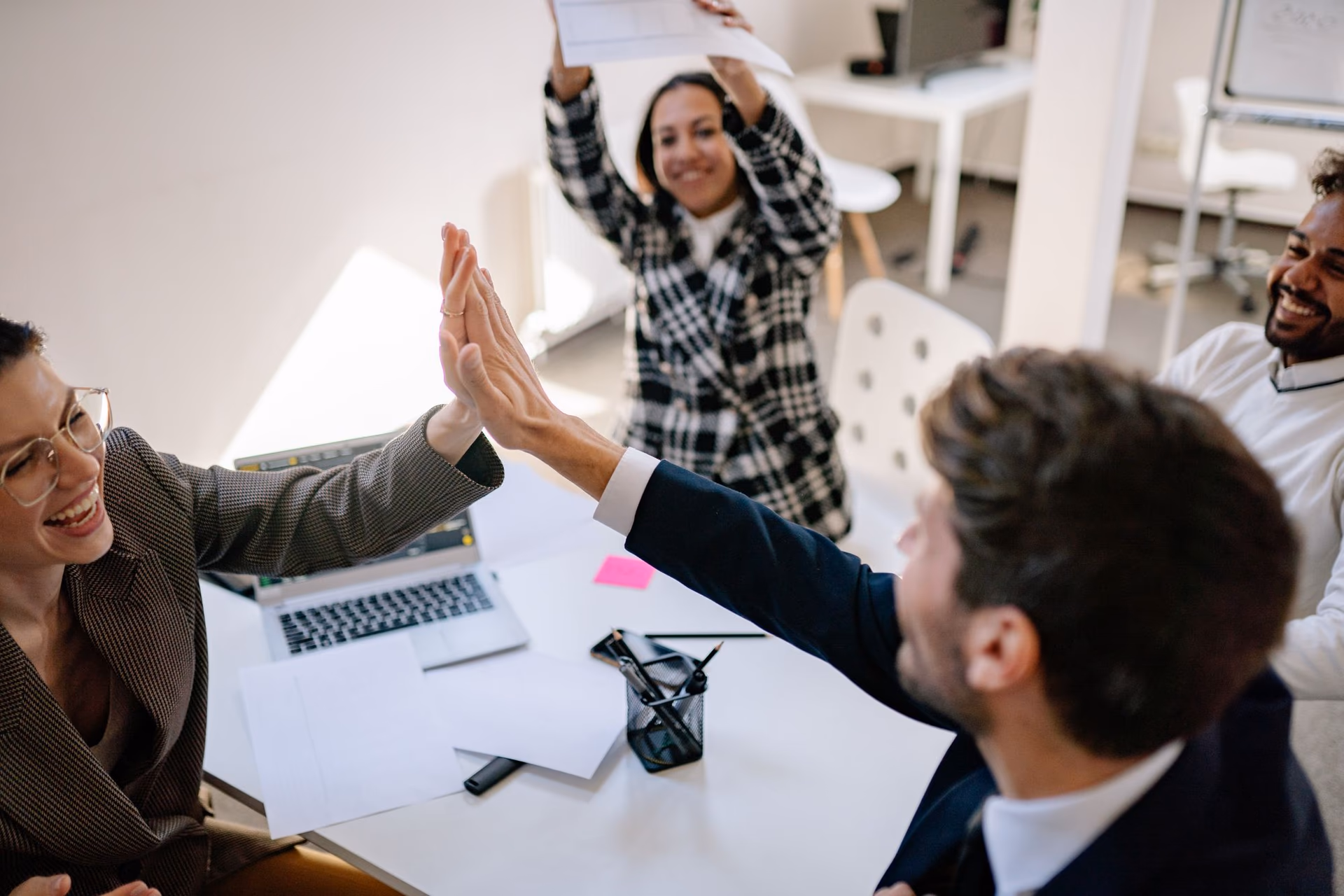 A team of coworkers high-fiving in celebration around an office desk